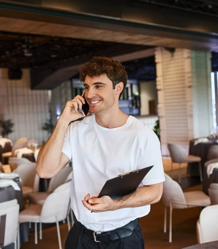 smiling-event-organizer-with-clipboard-talking-on-smartphone-near-festive-tables-in-banquet-hall.jpg